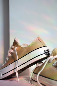 Close-up of beige sneakers with rainbow reflections on a white background, enhancing a fashion-forward look.