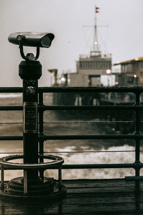 Free Moody view of a telescope on Santa Monica Pier with an ocean backdrop and overcast sky. Stock Photo