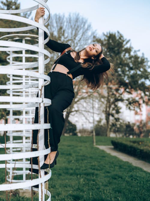 Woman in Black Clothes Posing on Bars at Park