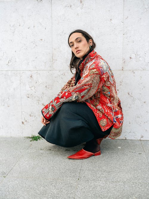 Young Woman in a Patterned Jacket Crouching on a Sidewalk 