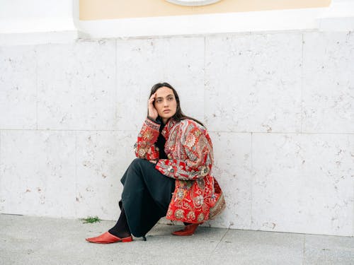 Young Woman in a Patterned Jacket Crouching on a Sidewalk 