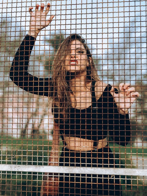 Woman Posing with Arm Raised behind Fence Net