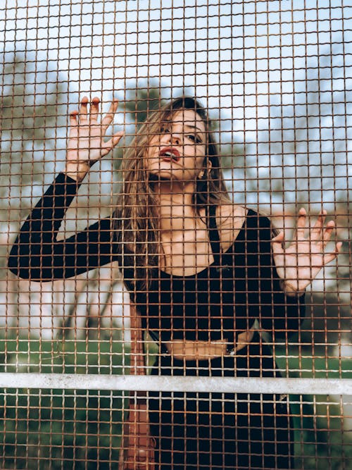 Woman in Black Clothes Standing with Hands Raised behind Fence