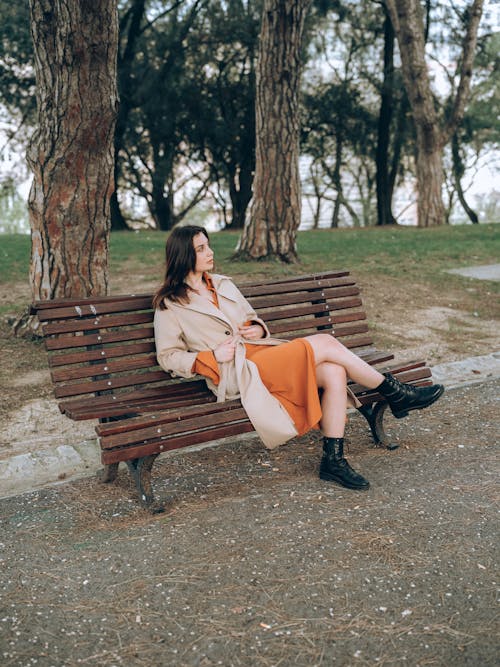 Woman in Trench Sitting on Bench at Park