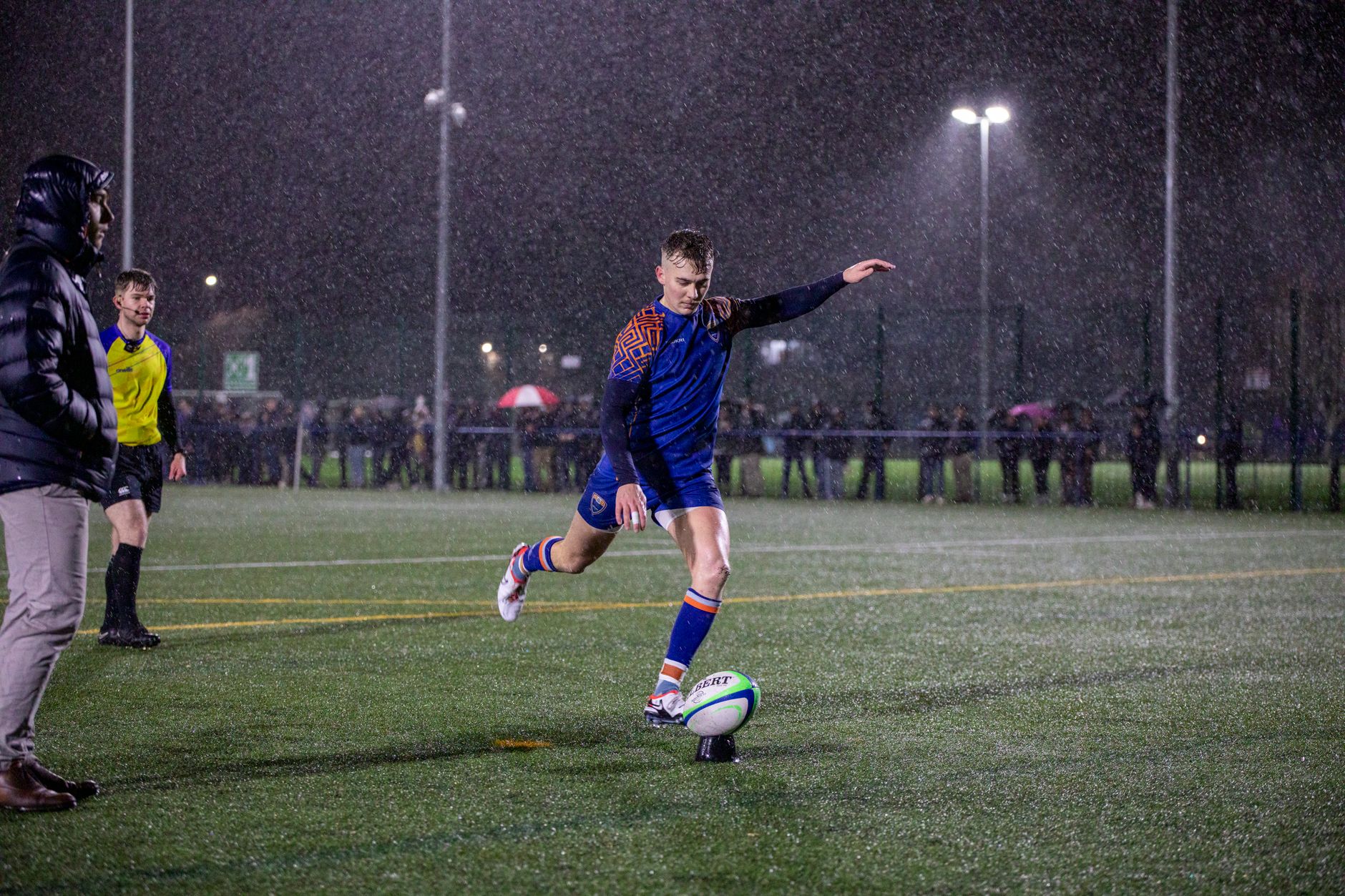 Dynamic shot of a rugby player kicking the ball during a night match in the rain at a Manchester stadium.
