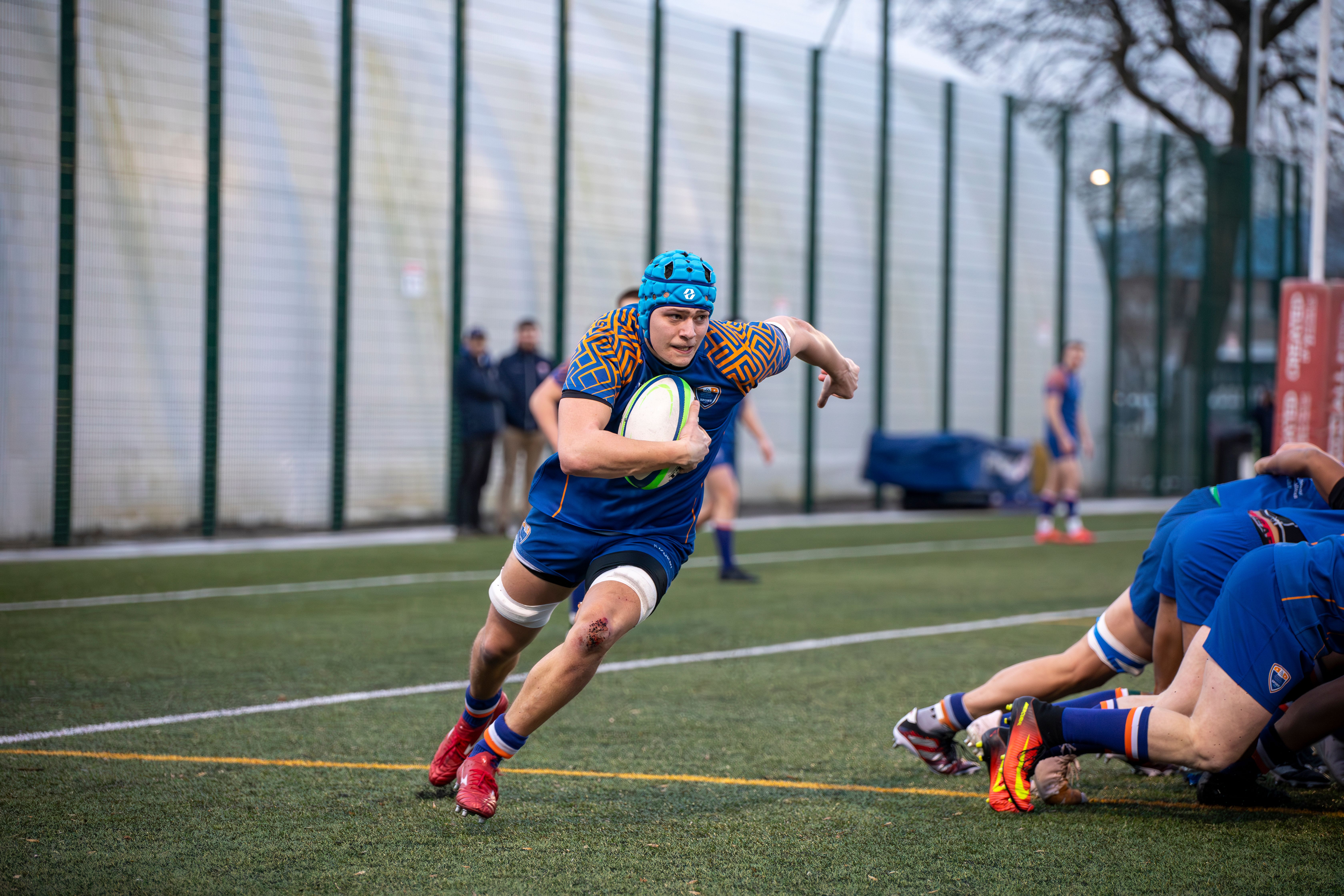Dynamic rugby action shot featuring a player running with the ball at a match in Manchester, England.
