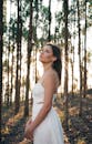 阳光明媚的森林中，一位身穿白色连衣裙的年轻女子优雅地摆出姿势，营造出迷人的场景