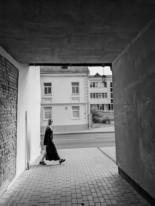 Black and White Photo of a Woman Walking on a Sidewalk in City 