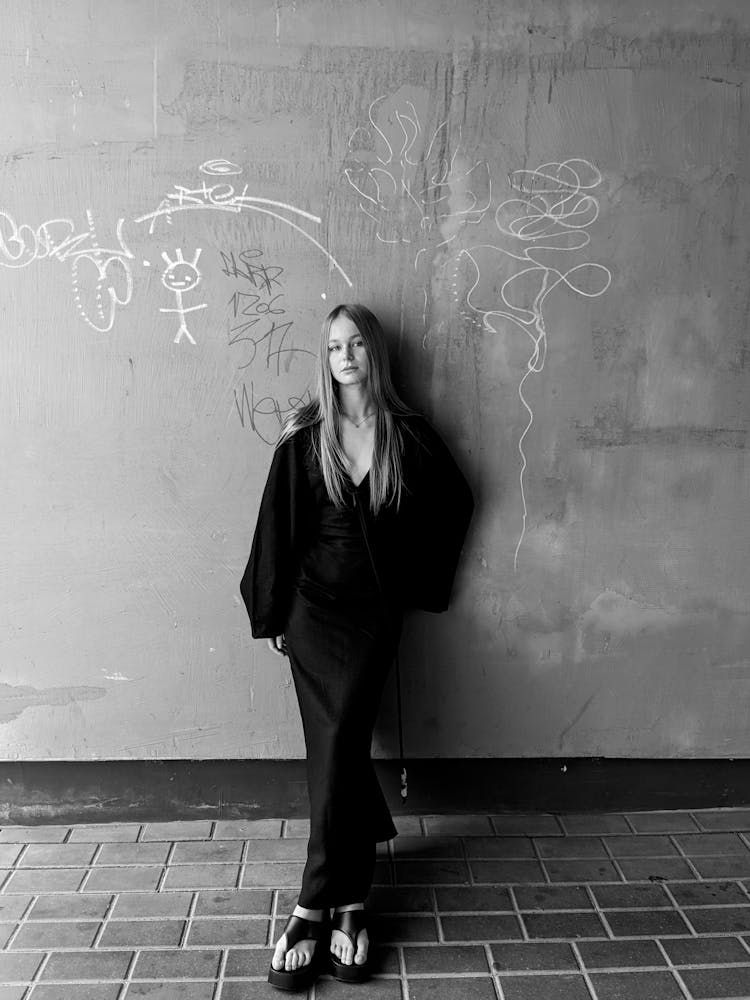 Young Woman In A Dress Standing Against A Wall Of A Building In City 