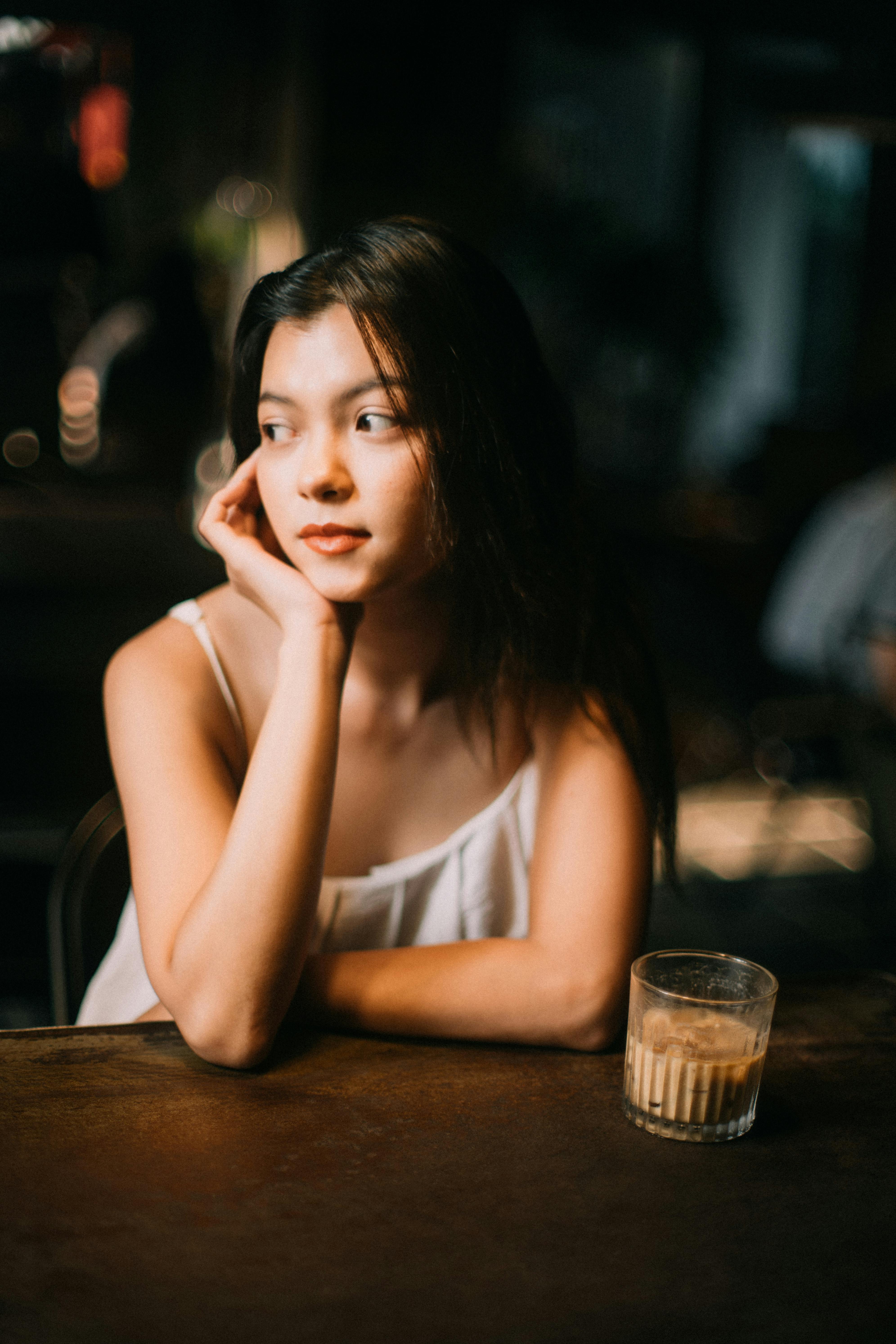 Woman sitting in a cafe, resting her chin on her hand, with a drink on the table.