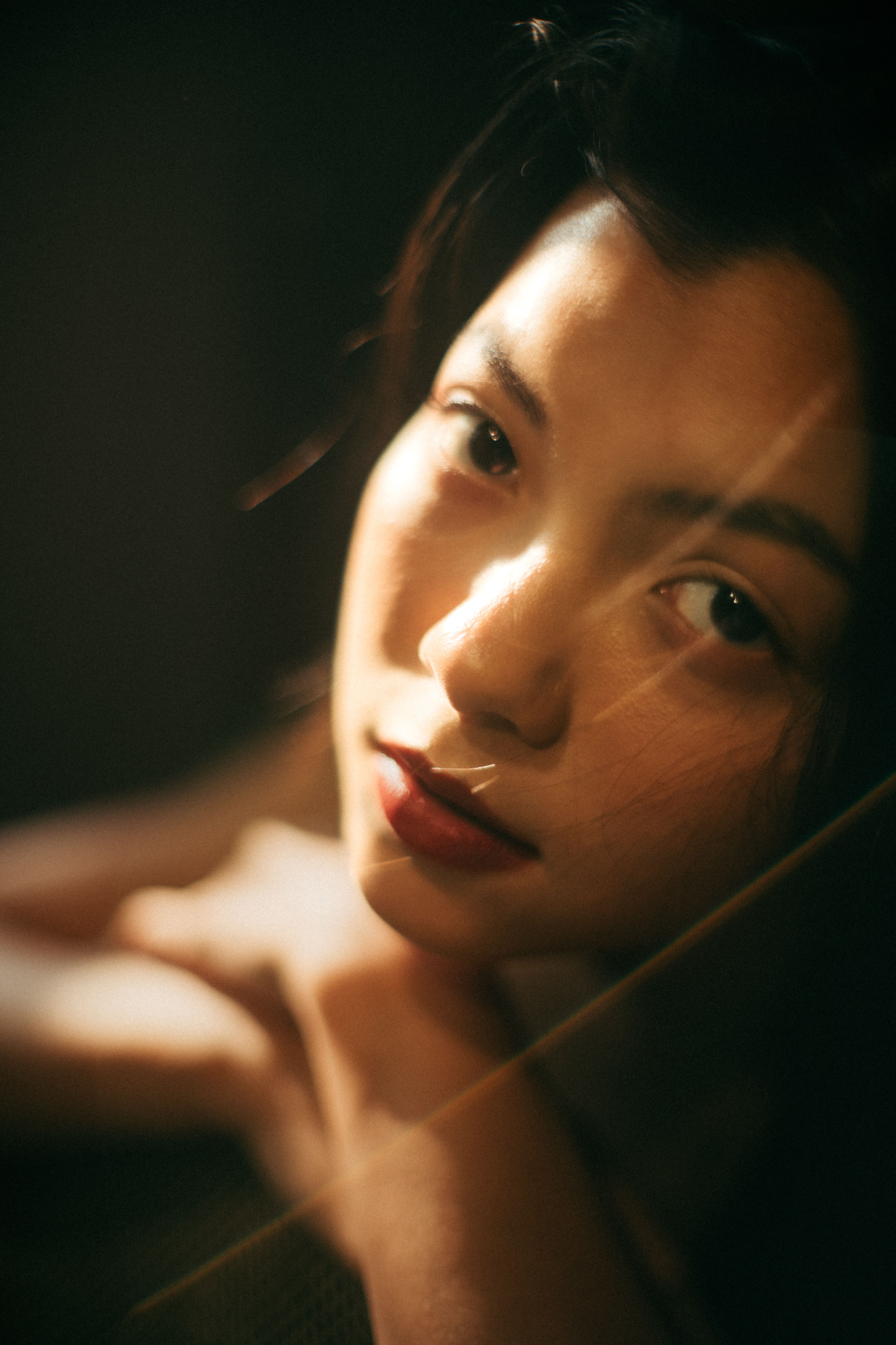 Artistic portrait of a woman with red lipstick and sunlight casting dramatic shadows on her face.