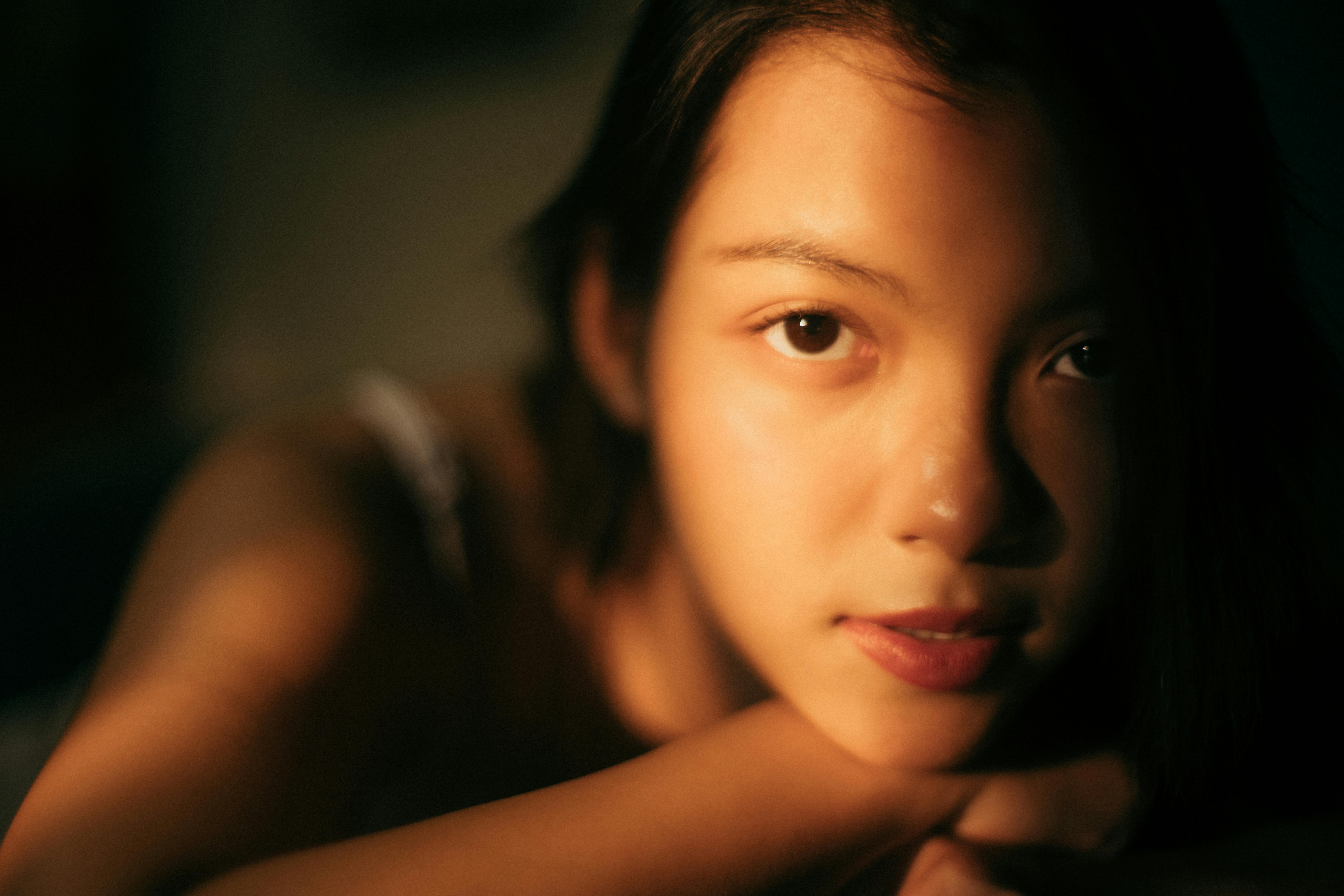 Close-up portrait of a young Asian woman in warm lighting, evoking a serene and introspective mood.