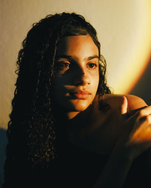 Free A young woman with curly hair in a thought-provoking, shadowed portrait. Stock Photo
