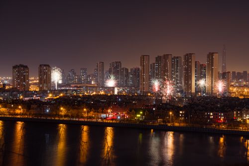 Free A splendid urban cityscape with fireworks lighting up the night sky over tall buildings reflecting in a river. Stock Photo