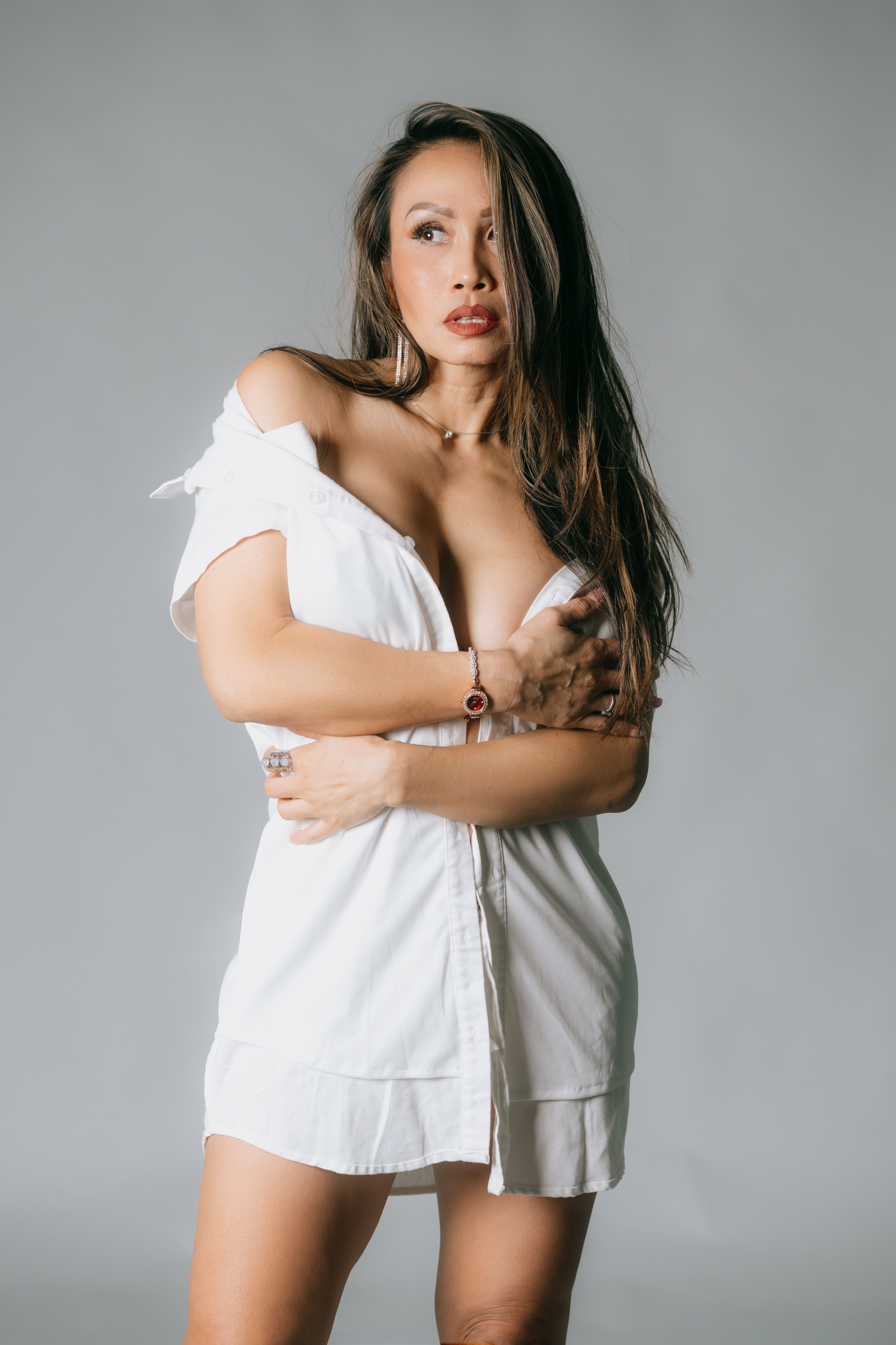 Studio portrait of a fashionable woman in a white shirt on a gray background.