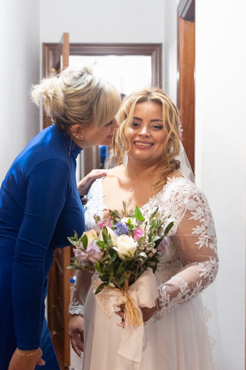A woman in a blue dress is hugging a bride