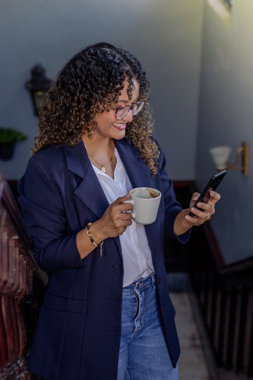 A woman in a suit holding a cup of coffee and looking at her phone