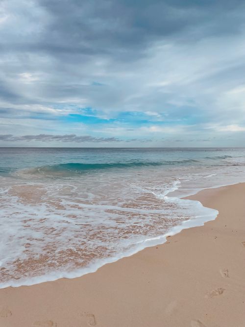 Free Peaceful beach scene with gentle waves and a cloudy sky, perfect for travel or relaxation themes. Stock Photo