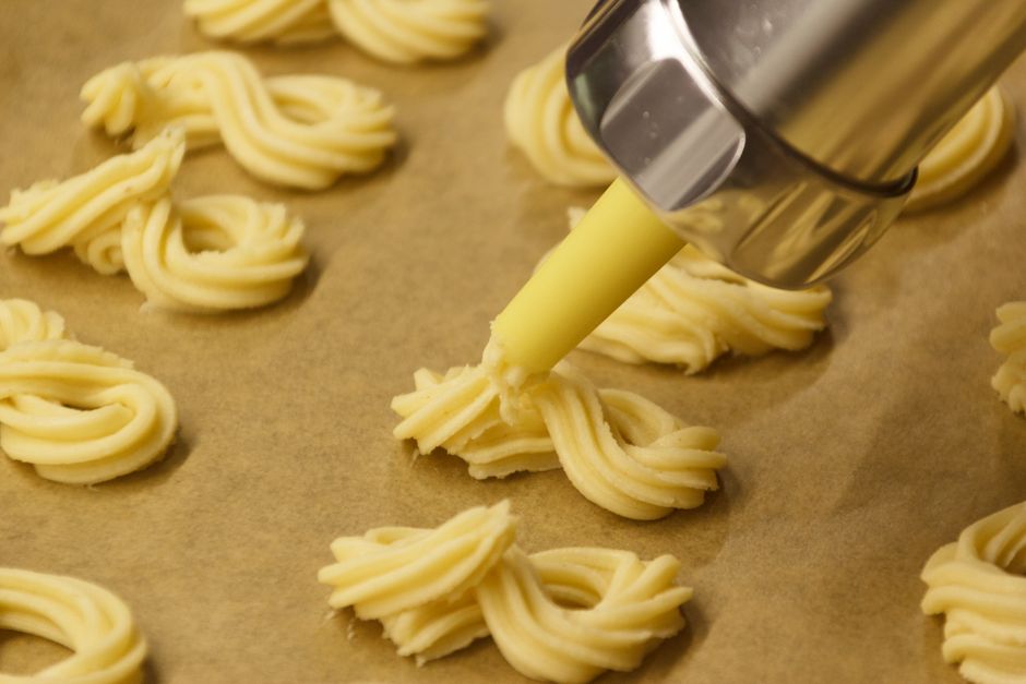 Close-up of cookie dough being piped into swirls on parchment paper using a pastry bag.