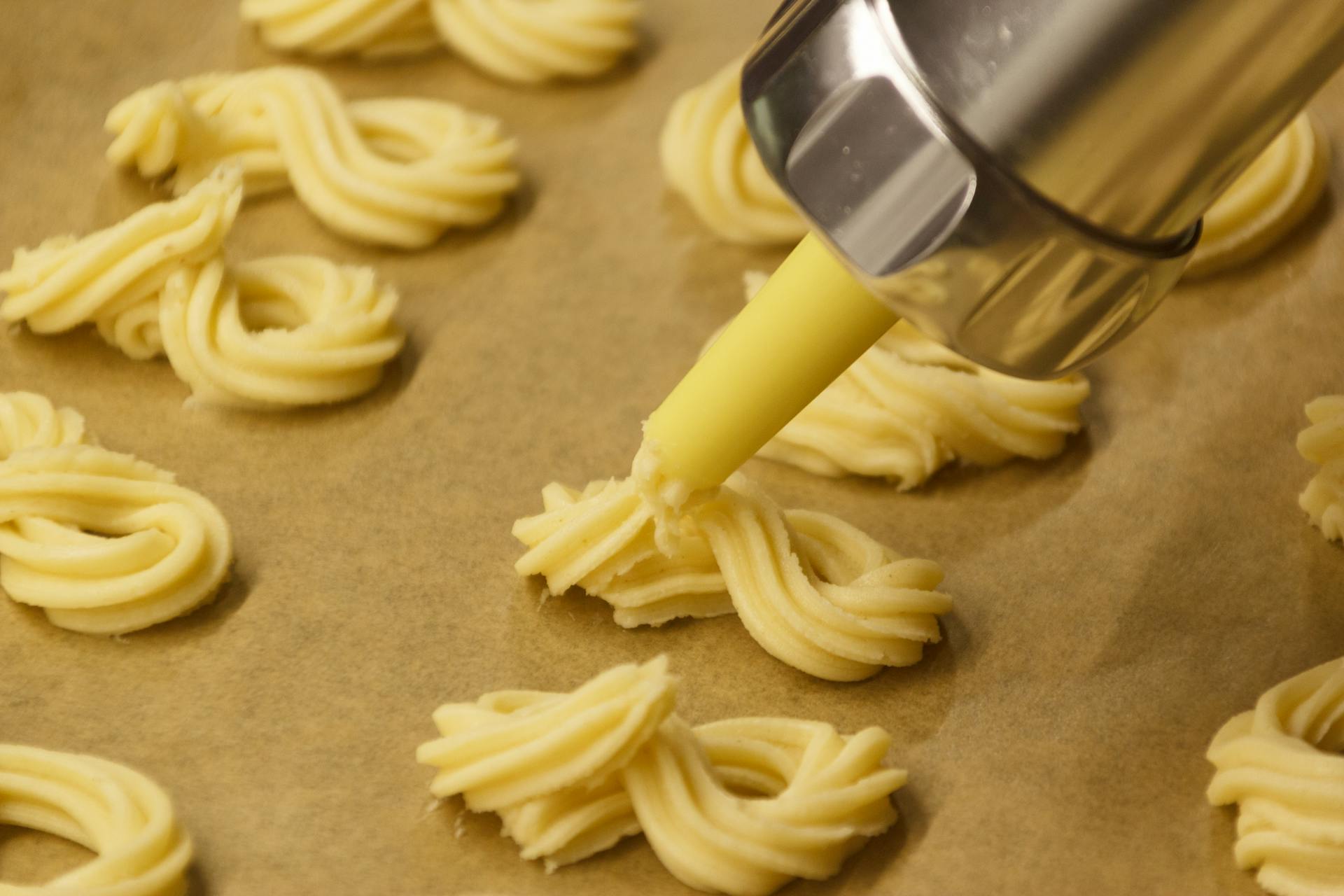 Close-up of cookie dough being piped into swirls on parchment paper using a pastry bag.