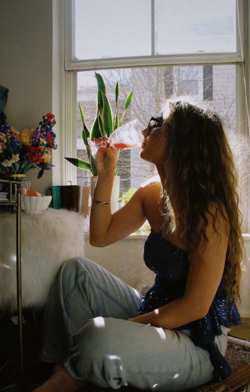 Free Young woman enjoying a refreshing drink by the window with sunlight streaming in. Stock Photo