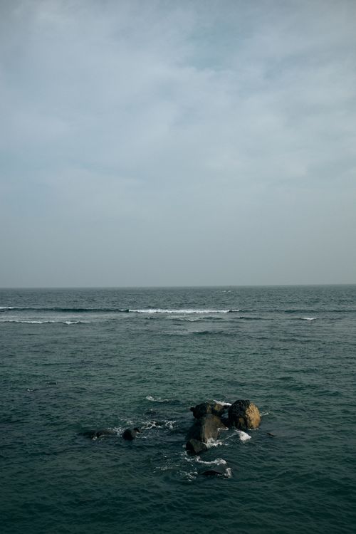 Free Peaceful ocean view featuring a rocky outcrop under a cloudy sky. Stock Photo