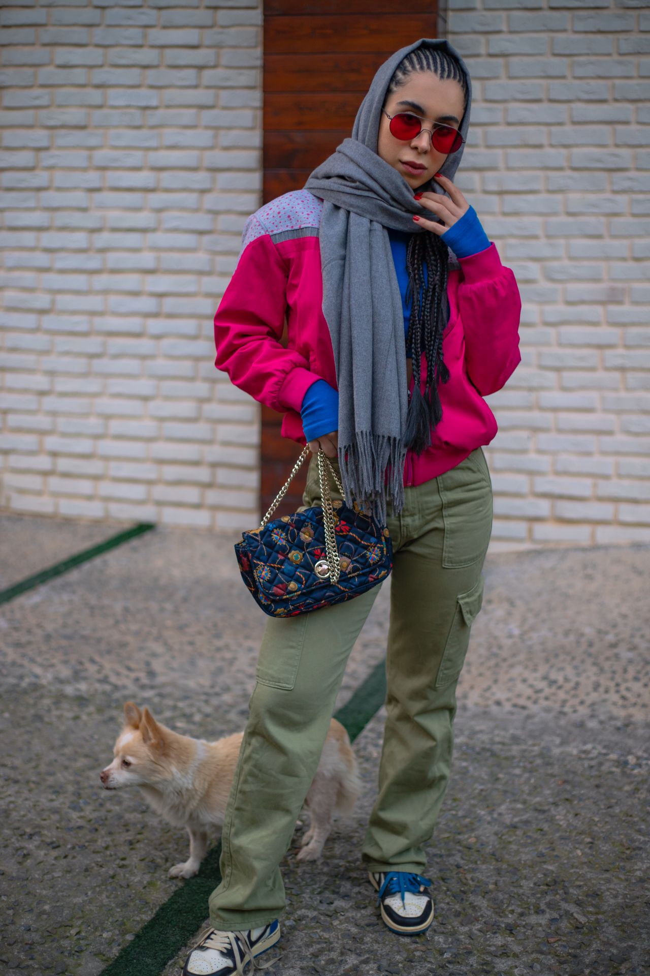 Woman in olive cargo pants, a pink jacket, and sneakers with a small dog