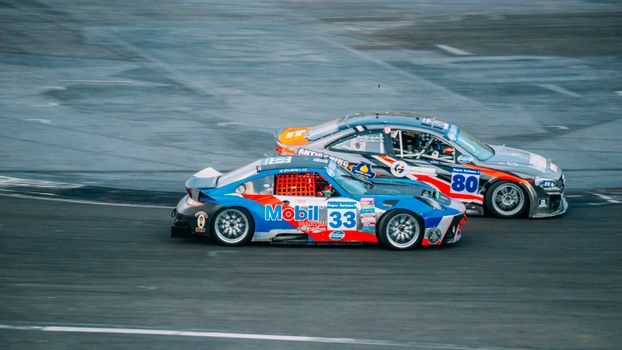 Two high-speed cars racing closely on an asphalt track during a thrilling event.