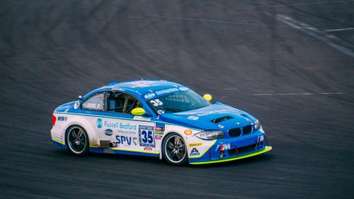 Free A blue race car speeding on the asphalt track during a daytime race event. Stock Photo