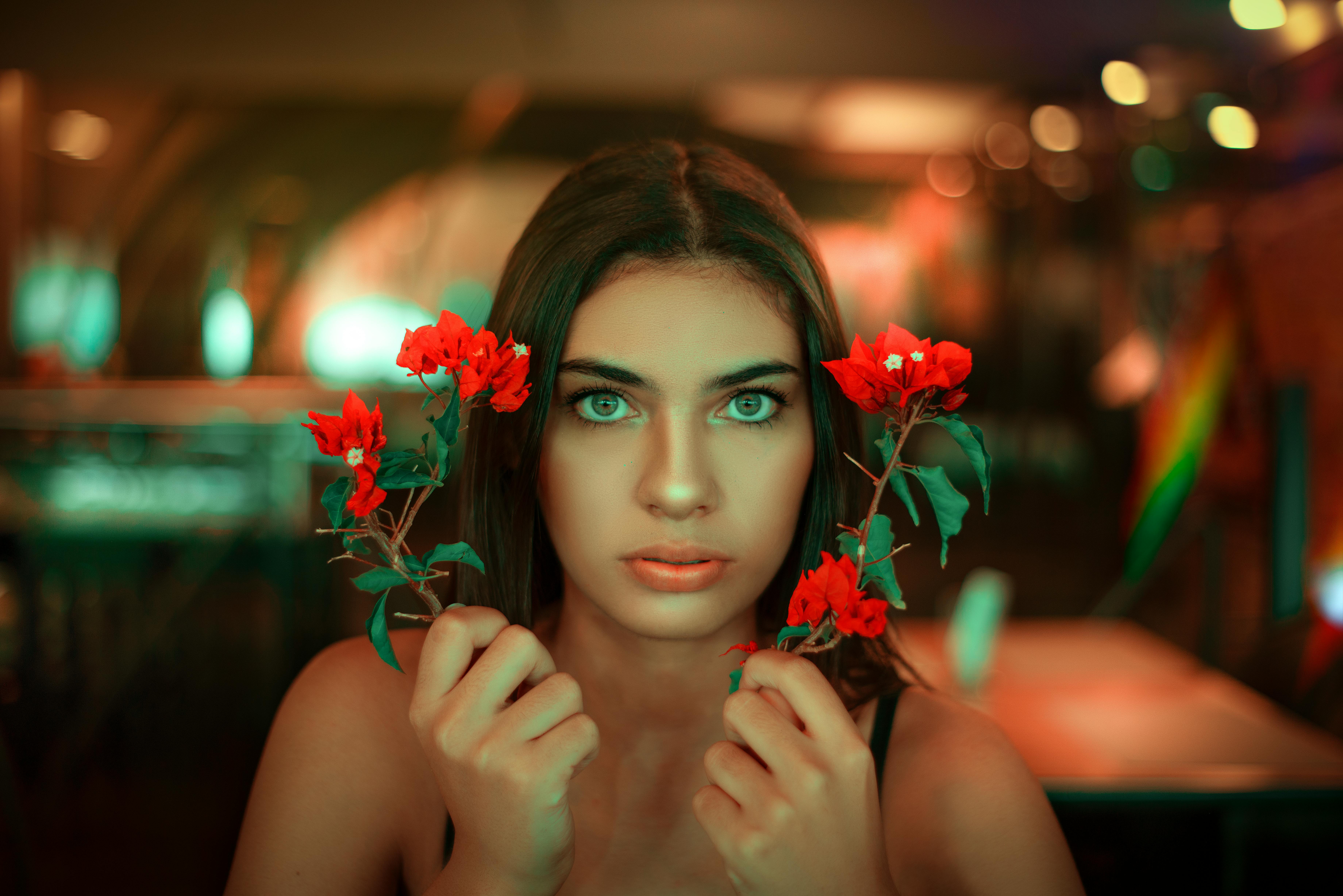 A striking portrait of a woman holding vibrant red flowers indoors.