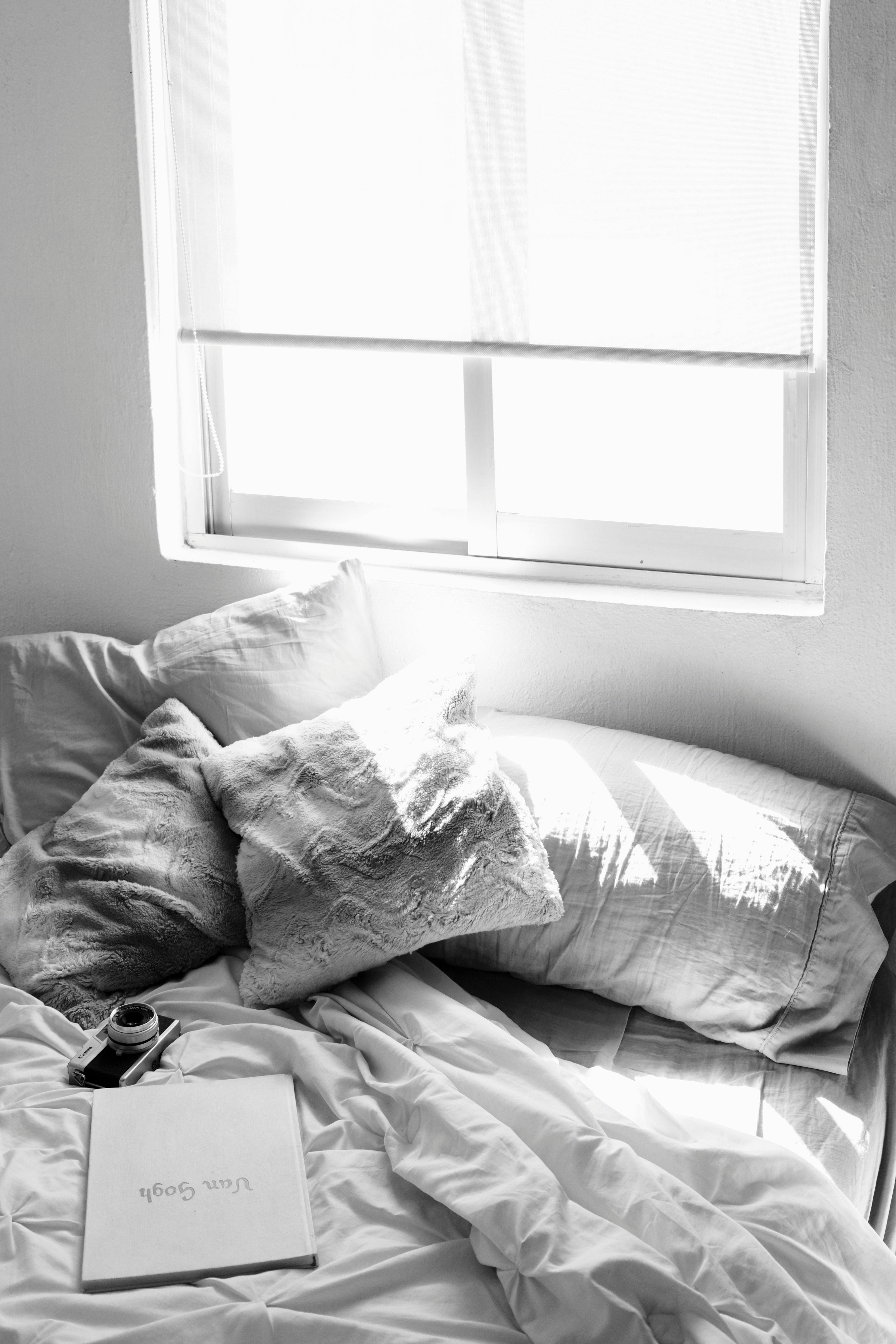 Black and white photo of a cozy bedroom with soft pillows, a window view, and a morning coffee.