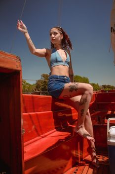 Stylish woman enjoying sunny day on a wooden boat, showcasing tattoos and summer fashion.