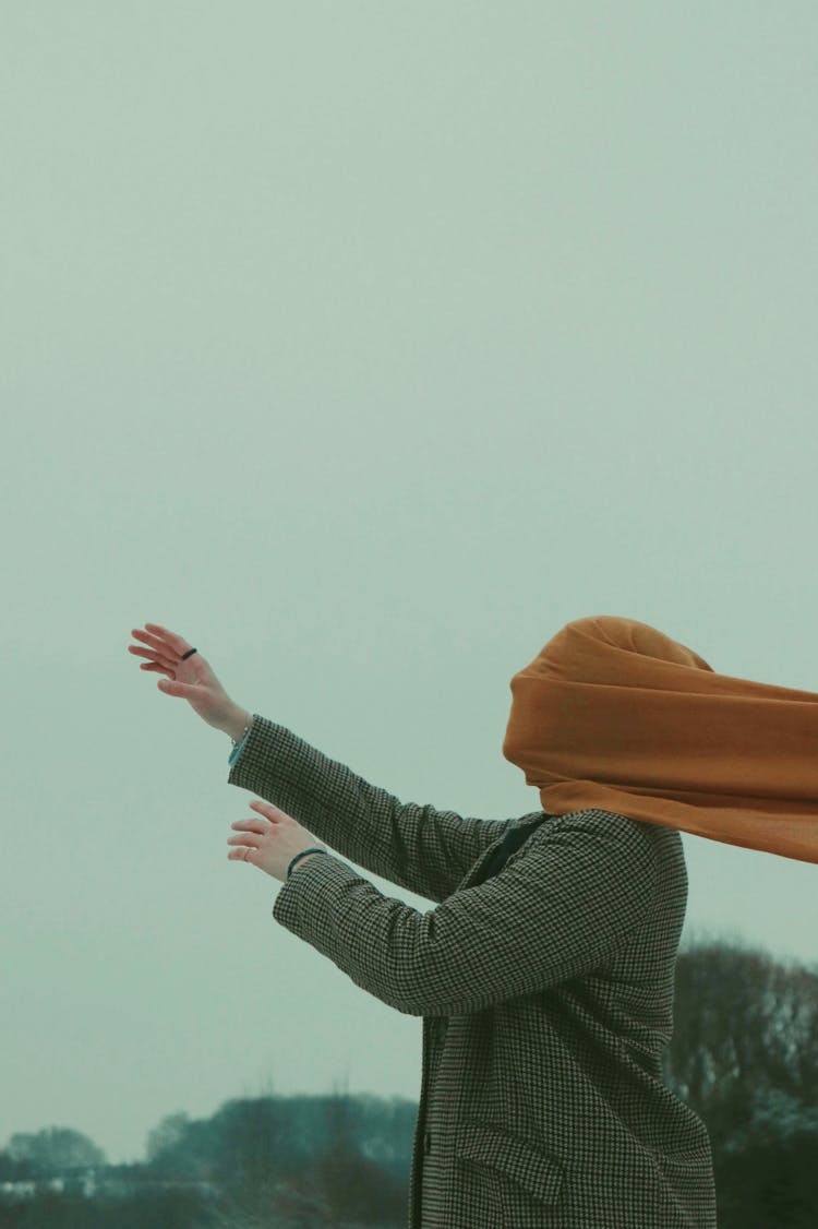 Woman Standing Outside With Her Arms Stretched Out And Face Covered With Yellow Fabric 