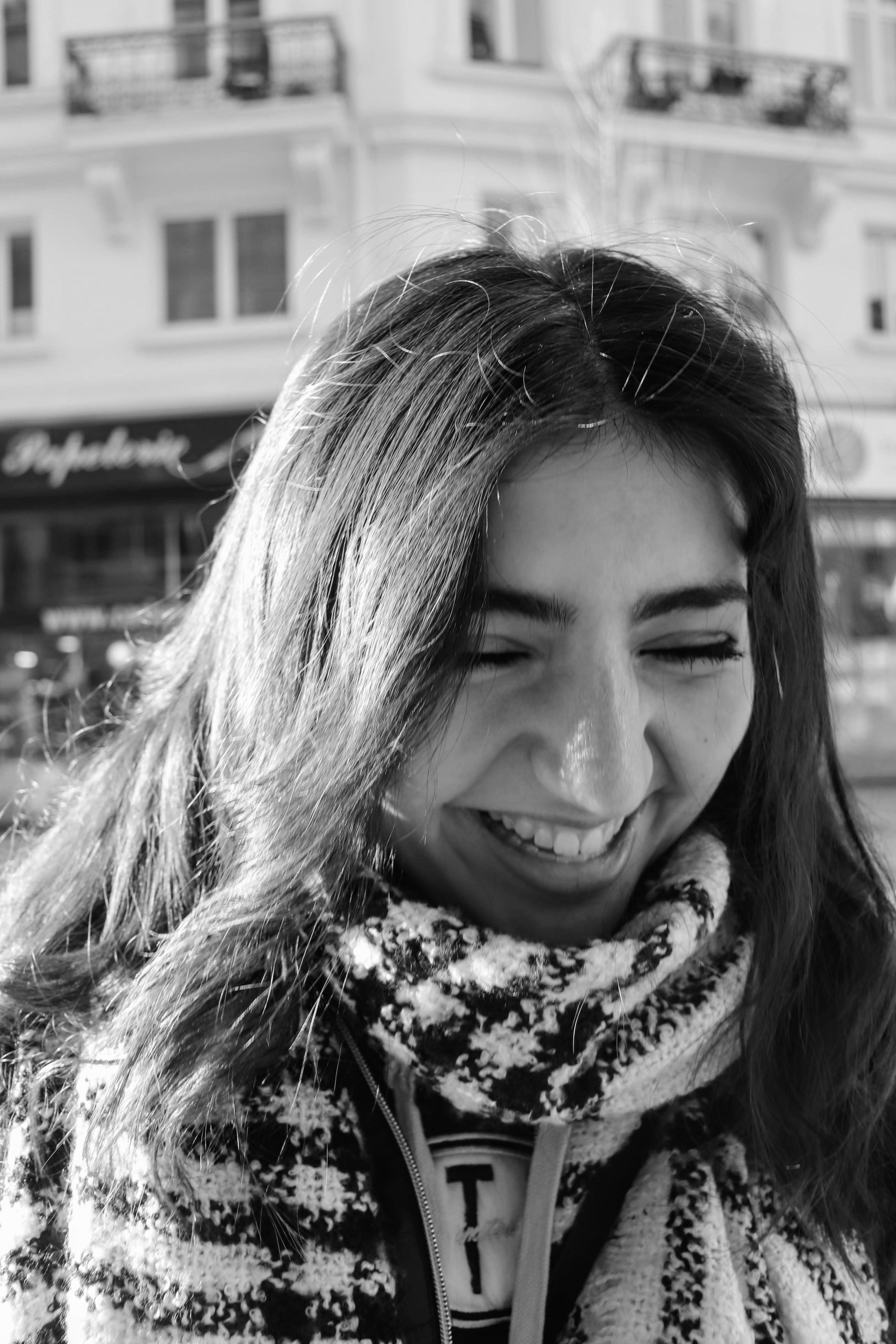 A delightful black and white portrait of a woman with long hair, smiling warmly in an urban setting.