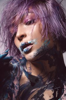 Artistic portrait of a woman with purple hair and abstract face paint, shot in a studio.