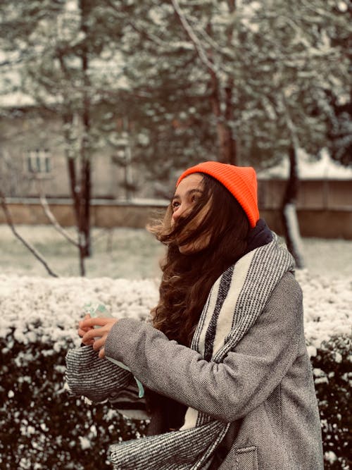 A woman in an orange hat and beanie is standing in the snow