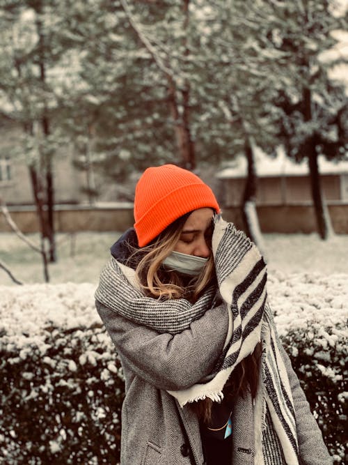 A woman wearing a hat and scarf is standing in the snow