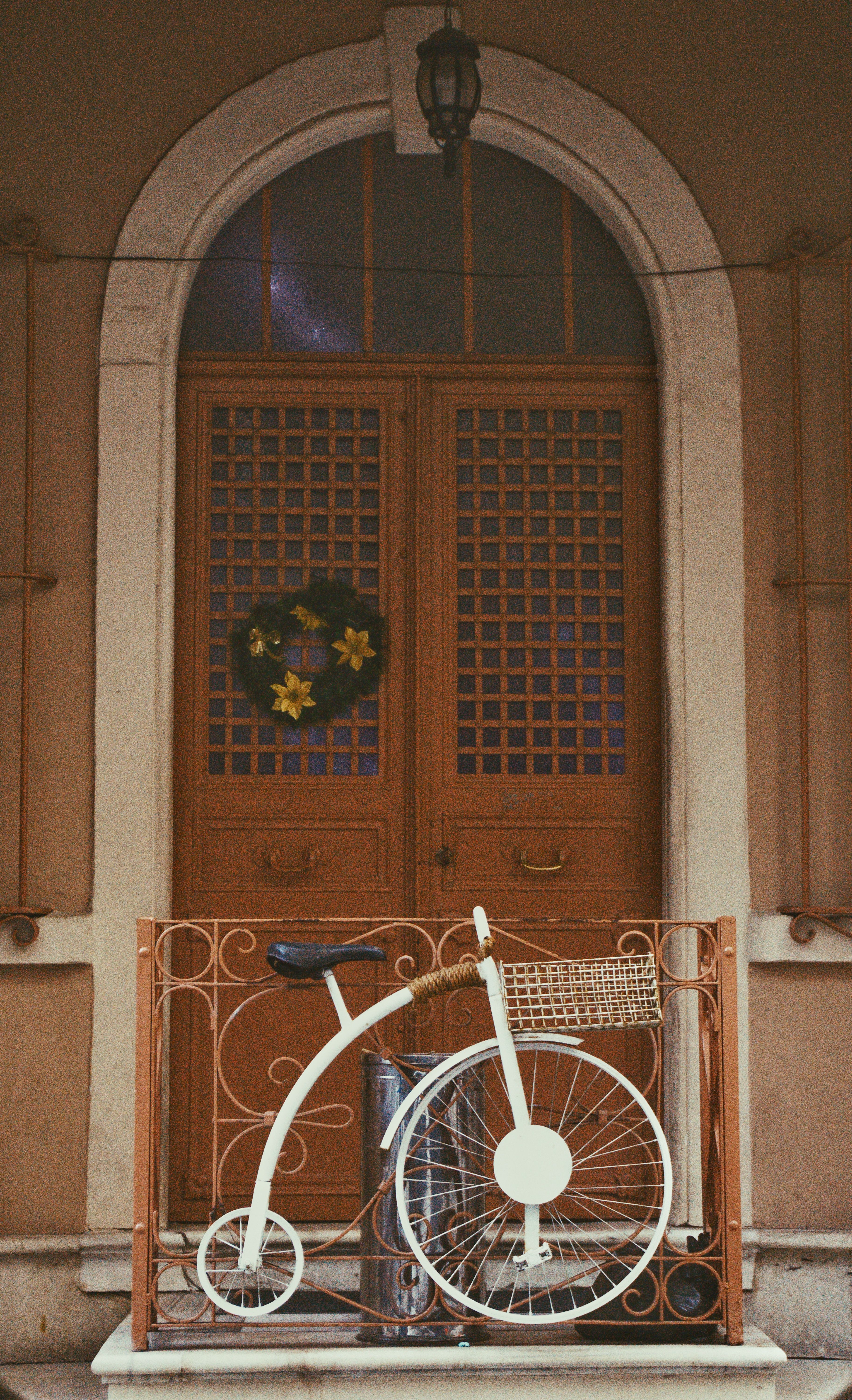 A vintage penny-farthing bicycle rests by a charming wooden door with a floral garland.