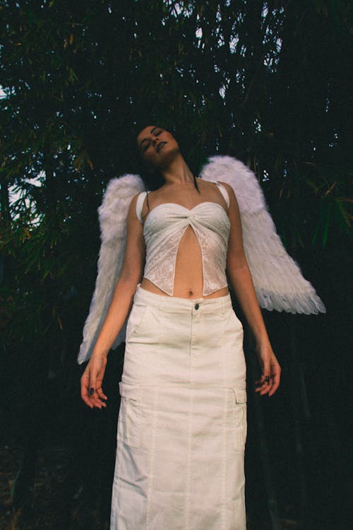 A woman in white with angel wings standing in the woods