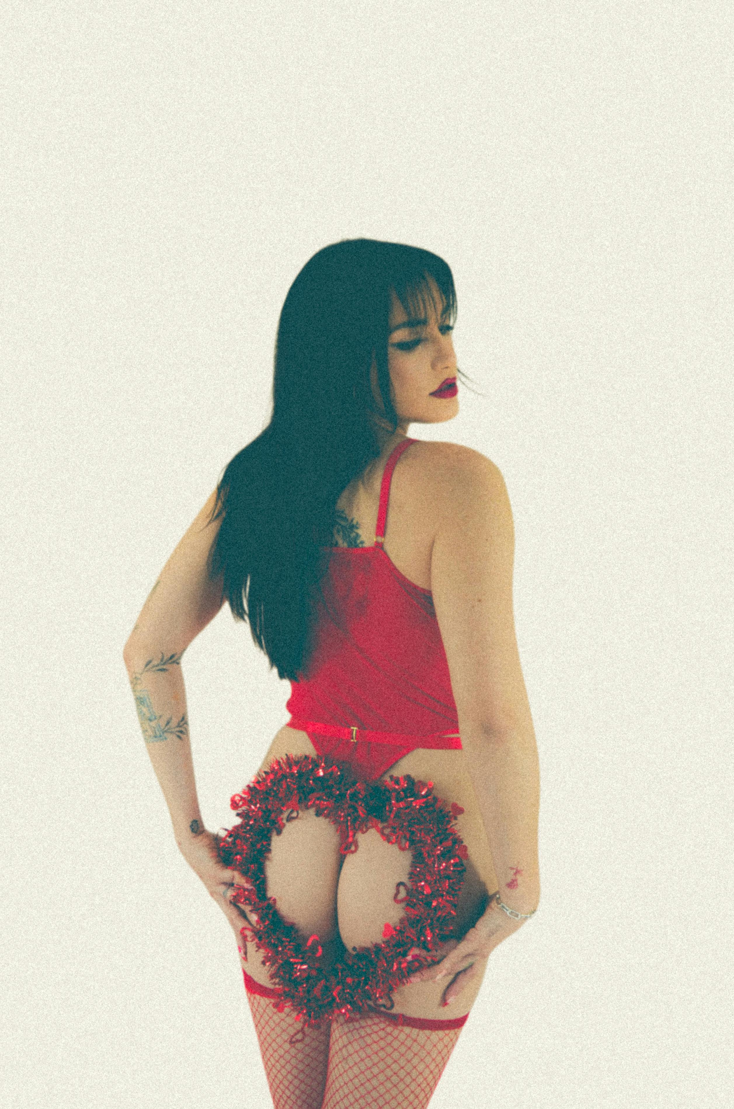 Model in red fashion attire posing with garland in studio setting.