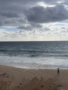 Man walks along Coogee Beach under a cloudy sky in Australia, capturing a serene coastal scene.