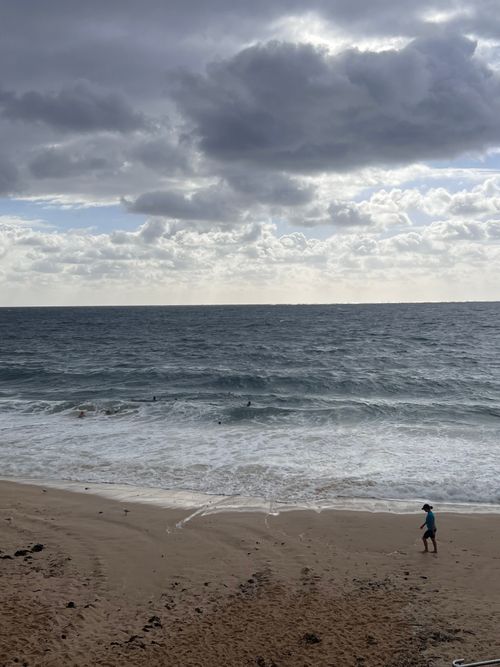Free Man walks along Coogee Beach under a cloudy sky in Australia, capturing a serene coastal scene. Stock Photo