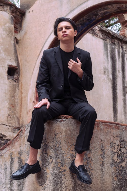 Young Handsome Man in Black Suit Sitting on Wall