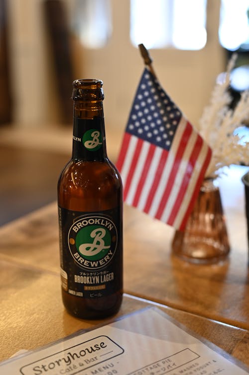 Brooklyn Beer in Glass Bottle by American Flag on Table