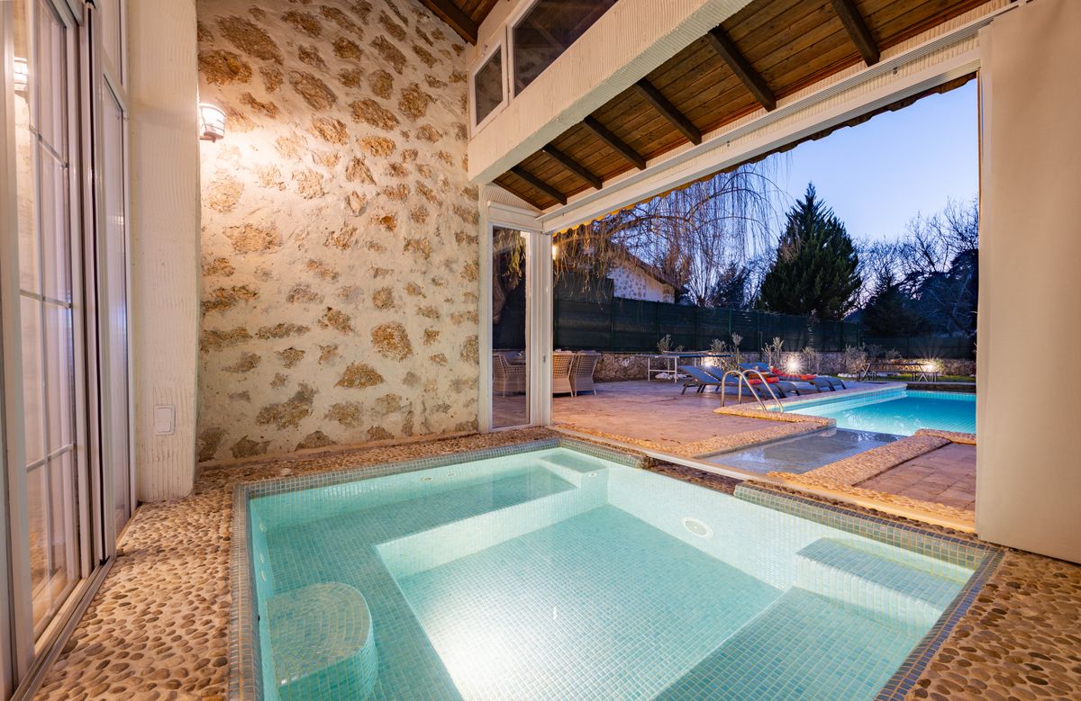 A softly lit plunge pool inside a stone-walled pavilion that opens onto a garden pool