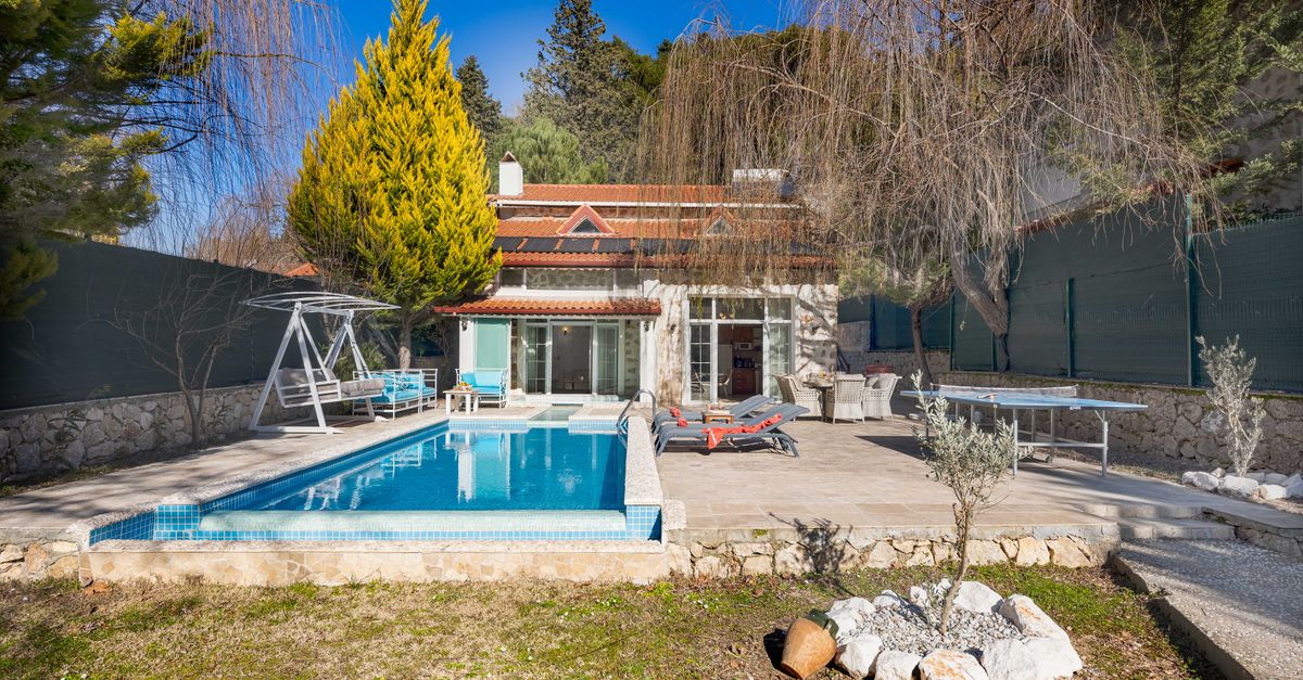 Beautiful luxury villa with a swimming pool, sunbeds, and outdoor relaxation area surrounded by trees.