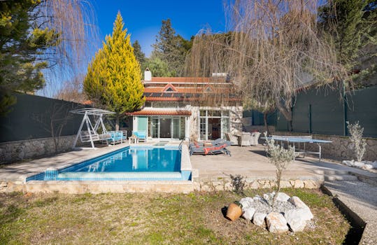 Beautiful luxury villa with a swimming pool, sunbeds, and outdoor relaxation area surrounded by trees.