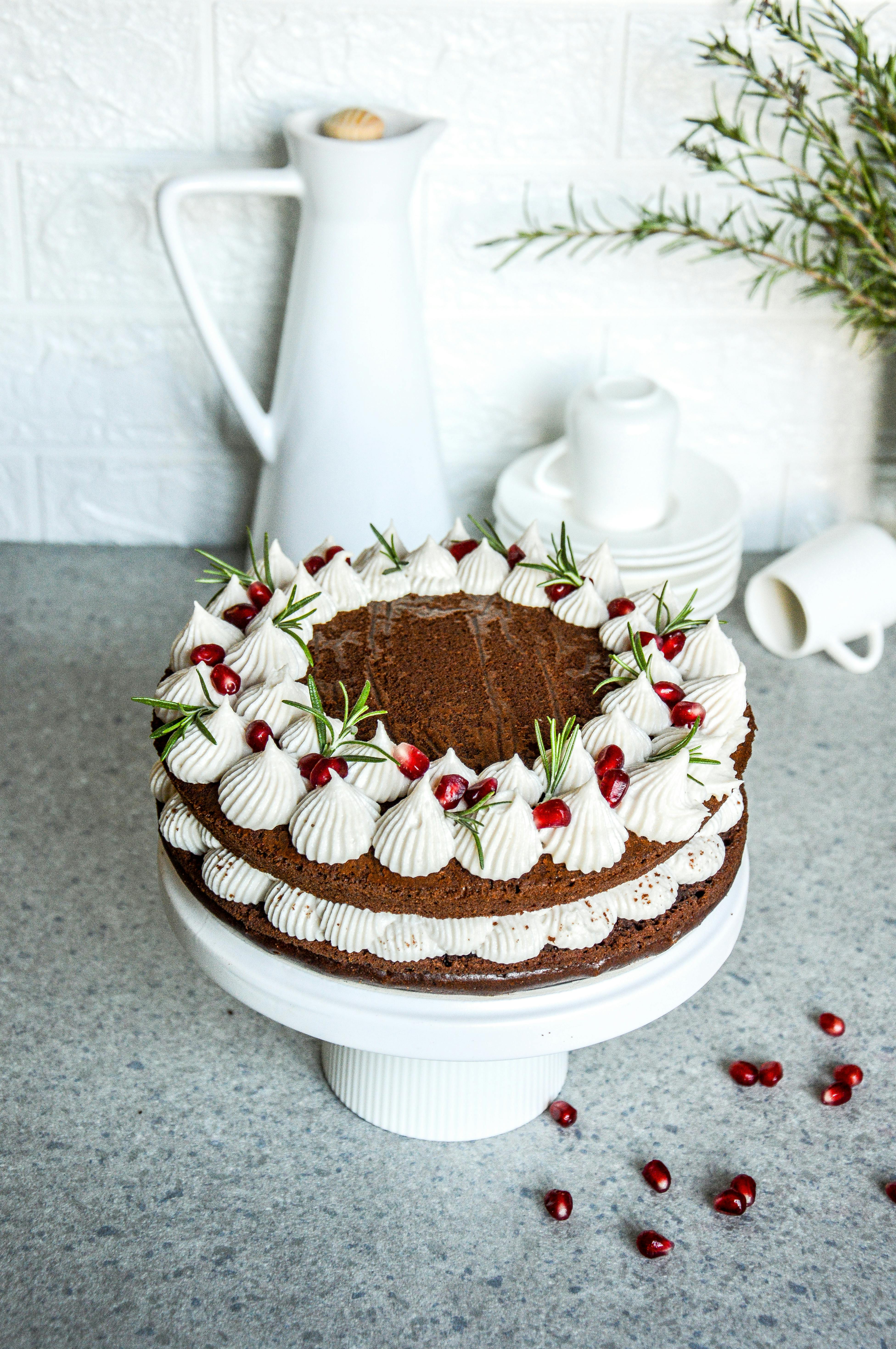 Delicious chocolate cake with cream and pomegranate seeds on a white stand.