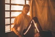 一位戴着眼镜的时尚男子坐在室内靠近窗户的位置，沐浴在金色时光的灯光下