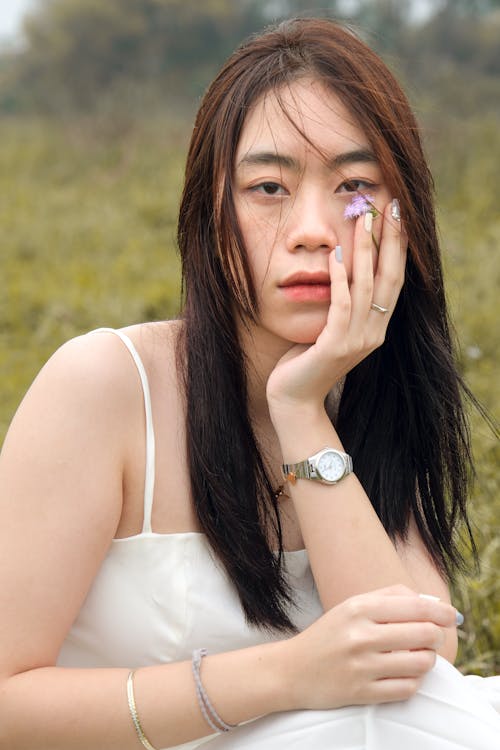 Portrait of Woman Sitting in White Dress and with Hand with Flower on Cheek